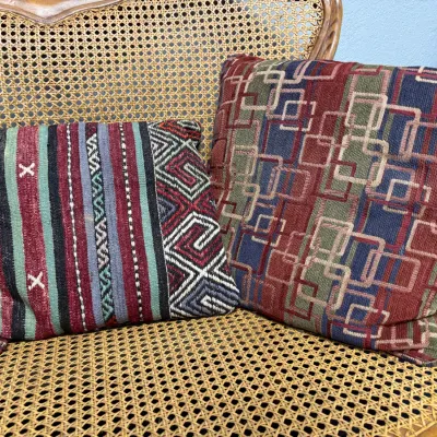 Sale Photo Thumbnail #671: Patterned throw pillows resting on a woven cane bench, including a geometric kilim style pillow and an interlocking square tapestry pillow.