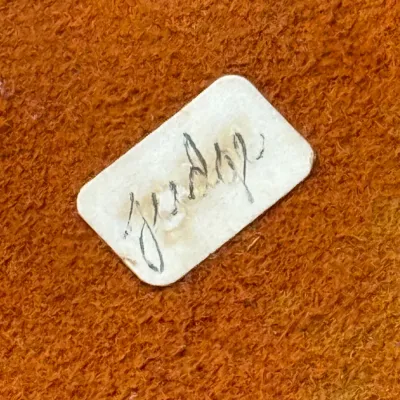 Sale Photo Thumbnail #410: Close-up detail of a handwritten maker's label reading 'Judith' attached to textured orange suede or leather.