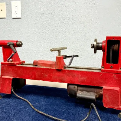 Sale Photo Thumbnail #560: Vintage red motorized mini wood lathe featuring a cast iron frame, adjustable tool rest, and chrome handwheels.