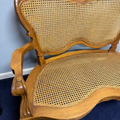 Sale Photo Thumbnail #673: Vintage carved wood bench with woven cane backrest and seat, featuring a contoured frame and carved armrests.