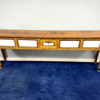 Sale Photo Thumbnail #273: Antique wooden long console or counter table featuring turned front legs, inset white panels, and a center drawer with a brass pull.