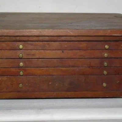 Vintage tabletop wooden cabinet featuring five shallow drawers with small brass knob hardware.