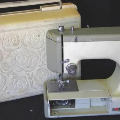 Vintage portable sewing machine in off-white and grey, complete with a rose-embossed hard carrying case showing light wear.