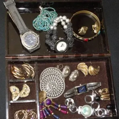 Open jewelry box containing an assortment of vintage costume jewelry, including wristwatches, beaded bracelets, clip-on earrings, and...