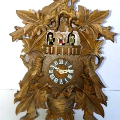 Vintage carved Black Forest cuckoo clock featuring hand-carved birds, oak leaves, and painted dancing figurines above the clock dial.