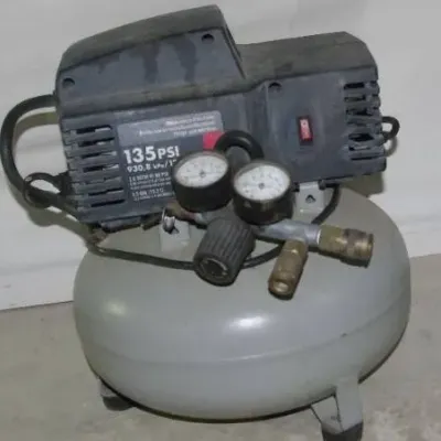 Portable 135 PSI pancake air compressor with dual pressure gauges, showing light cosmetic wear and dust from use.