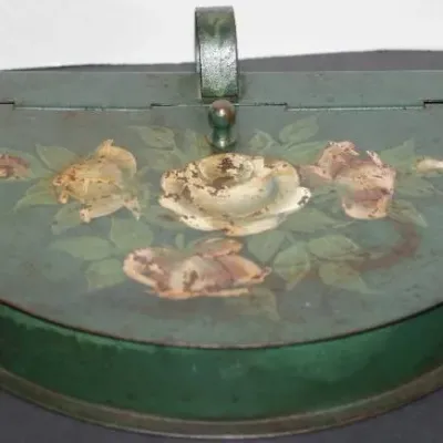 Vintage half-moon painted tin wall pocket or purse featuring a hand-painted floral motif against a dark green finish with visible patina...