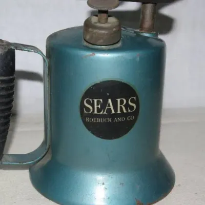 Vintage Sears, Roebuck and Co. teal gasoline blowtorch with a black ribbed handle.