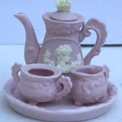 Miniature pink ceramic tea set featuring a teapot, sugar bowl, creamer, and matching tray with white cameo relief details.