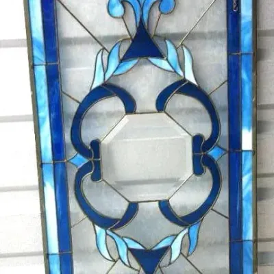 Rectangular stained glass window panel featuring a central bevel surrounded by intricate blue scrollwork and a matching border.