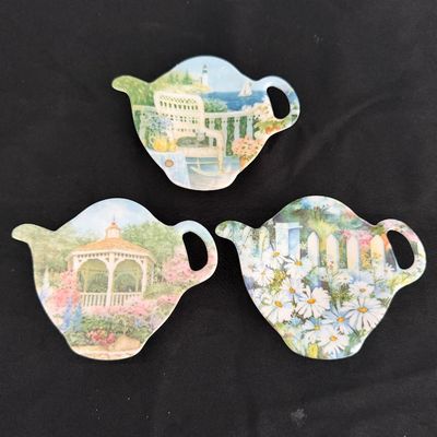 Sale Photo Thumbnail #21: Set of three teapot-shaped ceramic tea bag caddies featuring illustrated garden, coastal, and floral scenes.