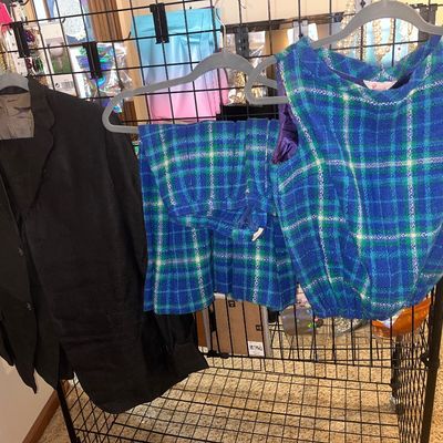 Vintage clothing items on hangers, including a black jacket and a vintage blue, green, and white plaid sleeveless top with matching...