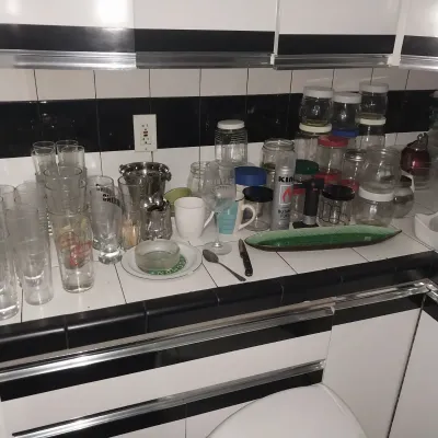 Sale Photo Thumbnail #15: Collection of assorted glassware, storage jars, mugs, and kitchenware displayed on a black and white tiled countertop.