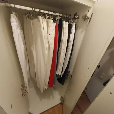 Sale Photo Thumbnail #21: A modern white wardrobe filled with various pairs of trousers, including white, red, and dark denim, hanging neatly on metal clip hangers.