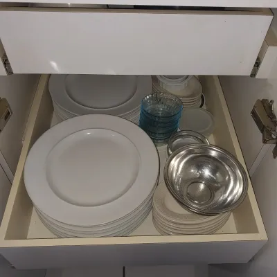 Sale Photo Thumbnail #19: A pull-out cabinet drawer filled with stacked white ceramic dinner plates, small glass preparation bowls, and a stainless steel bowl.