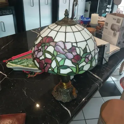 Sale Photo Thumbnail #7: Tiffany-style stained glass table lamp featuring a floral motif in shades of pink, purple, and green against a cream background, set on a cast bronze-tone base.