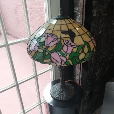 Sale Photo Thumbnail #6: Tiffany-style stained glass table lamp featuring a floral rose pattern on a cream background, mounted on a fluted bronze-finished metal base.