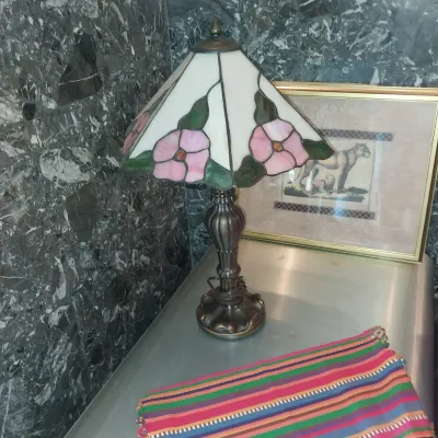 Sale Photo Thumbnail #5: Tiffany-style stained glass table lamp featuring a floral shade with pink flowers and green leaves on a dark metal base.