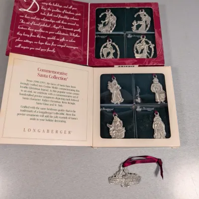 Sale Photo Thumbnail #137: Two sets of Longaberger pewter holiday ornaments in their original presentation boxes, including an Angel set and a Commemorative Santa Collection, accompanied by a loose sleigh ornament with ribbon.