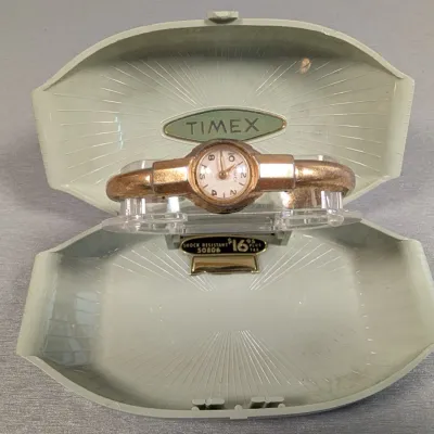 Sale Photo Thumbnail #375: Vintage Timex women's gold-tone bangle watch displayed in its original clamshell plastic presentation case with price tag.