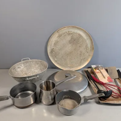 Sale Photo Thumbnail #26: Collection of vintage metal kitchenware, including aluminum saucepans, a colander, a round pizza pan, a Turkish coffee pot, and various cooking utensils.