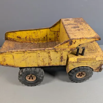 Sale Photo Thumbnail #335: Vintage Tonka yellow pressed steel dump truck, featuring heavy paint wear, rust patina, and black rubber tires.