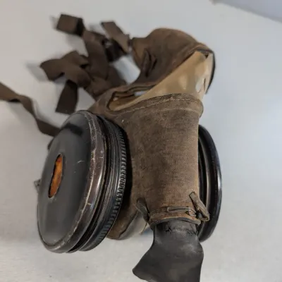Sale Photo Thumbnail #448: Vintage WWII-era military gas mask featuring dual filter canisters, fabric facepiece, and original head straps.