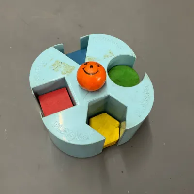 Sale Photo Thumbnail #253: Vintage Playskool light blue plastic shape sorter with colorful wooden blocks and an orange smiley face center knob.