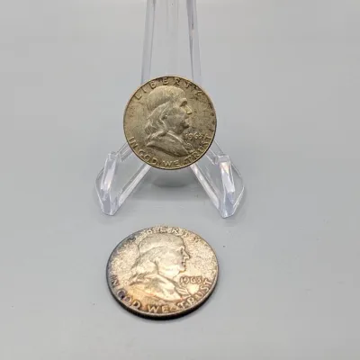Sale Photo Thumbnail #12: Two 1963 Benjamin Franklin silver half dollars, one displayed on a clear plastic stand.