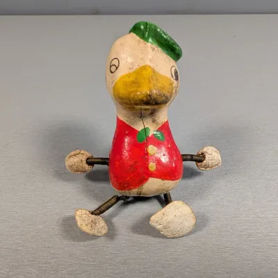 Sale Photo Thumbnail #373: Vintage painted papier-mâché or composition duck figurine with spring legs and arms, showing significant age wear, cracks, and paint loss.