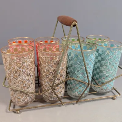 Sale Photo Thumbnail #161: Mid-century modern set of eight colorful highball glasses featuring a metallic checkered spatter pattern, displayed in a vintage brass-toned wire caddy with a wooden handle.