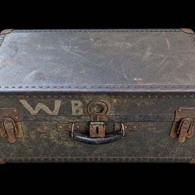 Sale Photo Thumbnail #171: Antique dark metal steamer trunk featuring riveted trim, brass latches, and stenciled initials 'W B' on the front.