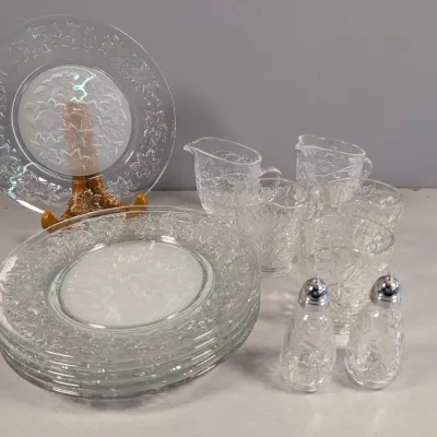 Sale Photo Thumbnail #127: Collection of clear pressed glass tableware featuring a poinsettia leaf pattern, including serving plates, creamers, small cups, and salt and pepper shakers.