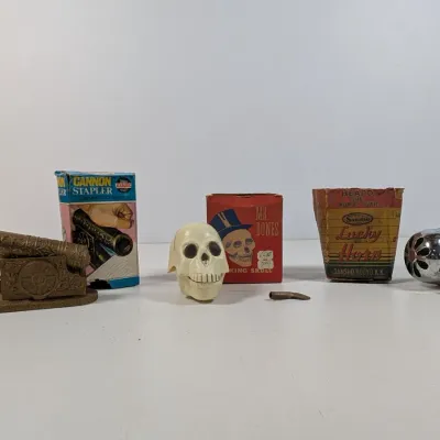 Sale Photo Thumbnail #407: Collection of vintage novelty items, including an Eagle Cannon stapler with original box, a Mr. Bones novelty skull, and a chrome bicycle horn.