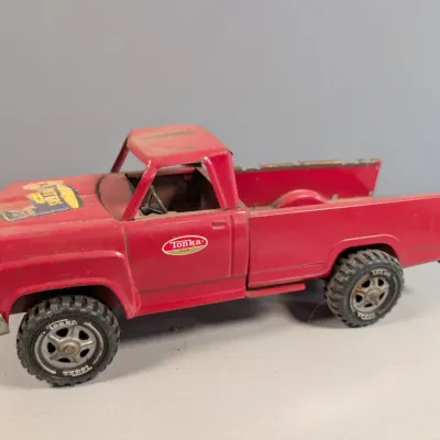 Sale Photo Thumbnail #166: Vintage red pressed-steel Tonka pickup truck toy with original side door decals, showing play wear and paint scuffs.