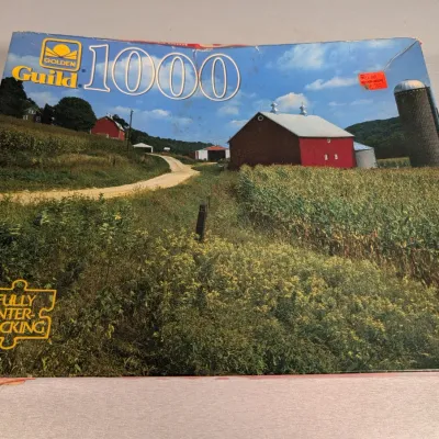 Sale Photo Thumbnail #306: Vintage Golden Guild 1000-piece jigsaw puzzle box featuring a rural farm landscape scene with red barns and a silo.