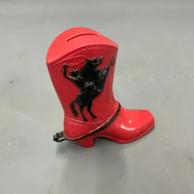 Sale Photo Thumbnail #273: Vintage red plastic cowboy boot bank featuring a black raised motif of a cowboy riding a bucking horse.