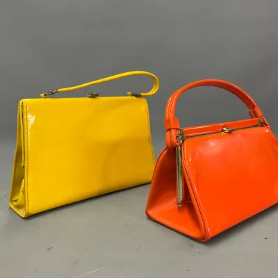 Sale Photo Thumbnail #284: Pair of vintage 1960s patent leather top-handle handbags in bright yellow and orange, both featuring classic clasp closures.