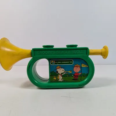 Sale Photo Thumbnail #406: Vintage 1970s Child Guidance Peanuts "Snoopy's Beagle Bugle" plastic toy in green and yellow, featuring graphics of Snoopy, Charlie Brown, and Woodstock.