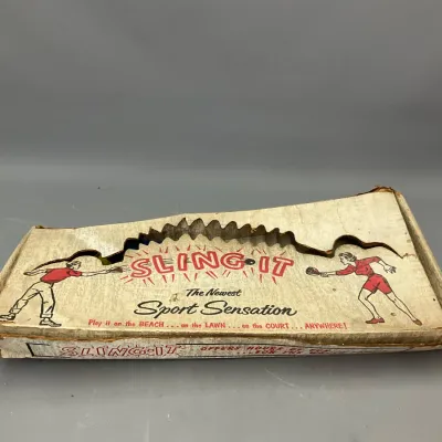 Sale Photo Thumbnail #214: Vintage Sling-It game in original illustrated cardboard box, showing heavy wear and damage along the upper edge.