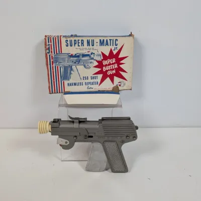 Sale Photo Thumbnail #48: Vintage Super Nu-Matic Jr. Paper Buster toy gun made of metal, complete with original illustrated packaging box.
