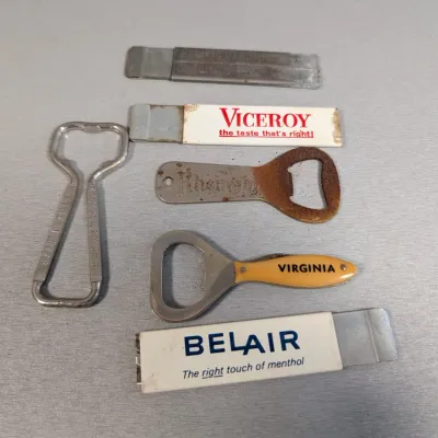 Sale Photo Thumbnail #30: Collection of vintage advertising bottle openers and pocket tools, including Viceroy, Belair, and Rheingold branding, showing varying degrees of wear and patina.