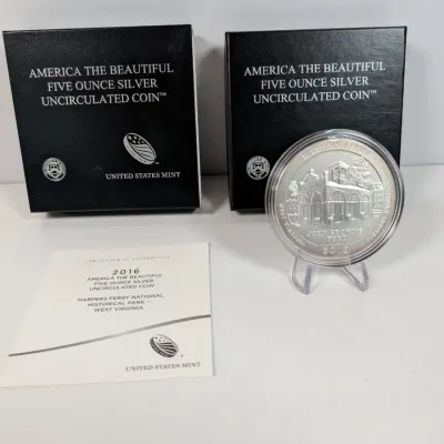 Sale Photo Thumbnail #6: 2016 America the Beautiful Harpers Ferry five-ounce silver uncirculated coin, displayed on a small plastic stand with its original US Mint presentation boxes and certificate of authenticity.