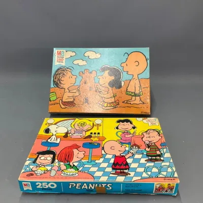 Sale Photo Thumbnail #106: Two vintage Milton Bradley Peanuts 250-piece jigsaw puzzle boxes featuring Charles Schulz artwork, including a beach scene and an ice cream parlor scene.