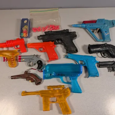 Sale Photo Thumbnail #321: Collection of vintage plastic toy guns and squirt guns, including space ray guns, Derringers, and cap pistols, alongside a bag of small plastic caps.