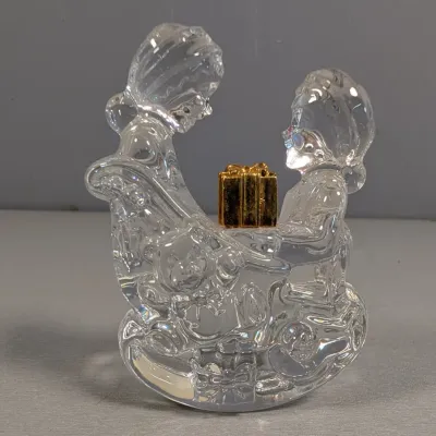 Sale Photo Thumbnail #138: Swarovski crystal Santa and Mrs. Claus figurine on a rocking horse base, featuring a small gold-tone present accent.