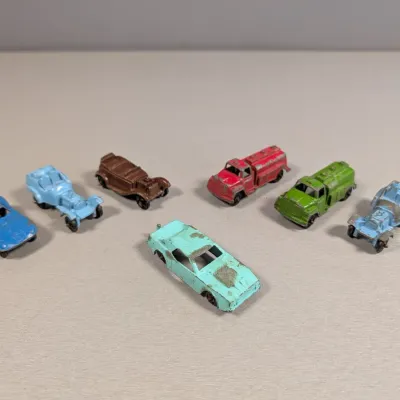 Sale Photo Thumbnail #355: Collection of seven vintage miniature die-cast and plastic toy vehicles, showing heavy paint wear and missing components consistent with age and play.