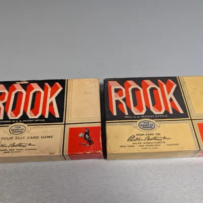 Sale Photo Thumbnail #384: Two vintage Parker Brothers Rook card game boxes showing light edge wear and age-related toning, featuring iconic Art Deco era red and black typography.