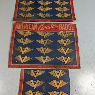 Sale Photo Thumbnail #359: Vintage World War II era American Aviator Badge display cards featuring gold-tone winged 'V for Victory' lapel pins mounted on original red, white, and blue cardboard backing.