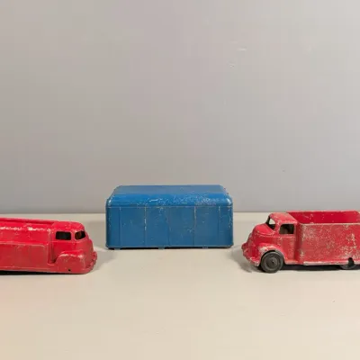 Sale Photo Thumbnail #354: Trio of vintage painted pressed steel toy vehicles, including two red trucks and a blue trailer, showing age-appropriate paint wear.